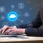 A professional illustration featuring a hiring manager at a workstation reviewing candidate profiles on a digital dashboard, surrounded by cloud icons, server nodes, and a floating checklist. A glowing brain symbol represents strategic decision-making, while the overlaid text reads "What Hiring Managers Should Know About Cloud Recruitment." The image conveys the strategic approach required for successful Cloud Recruitment in today's competitive tech landscape.