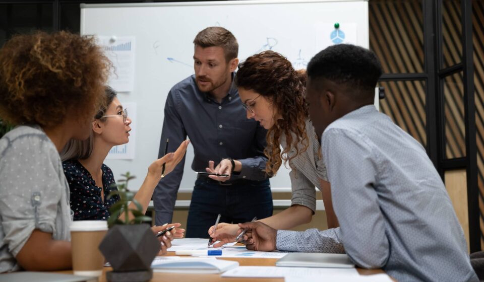 Diverse AWS team collaborating on cloud architecture with AWS service icons and deployment dashboards, highlighting the structure of a successful AWS Team