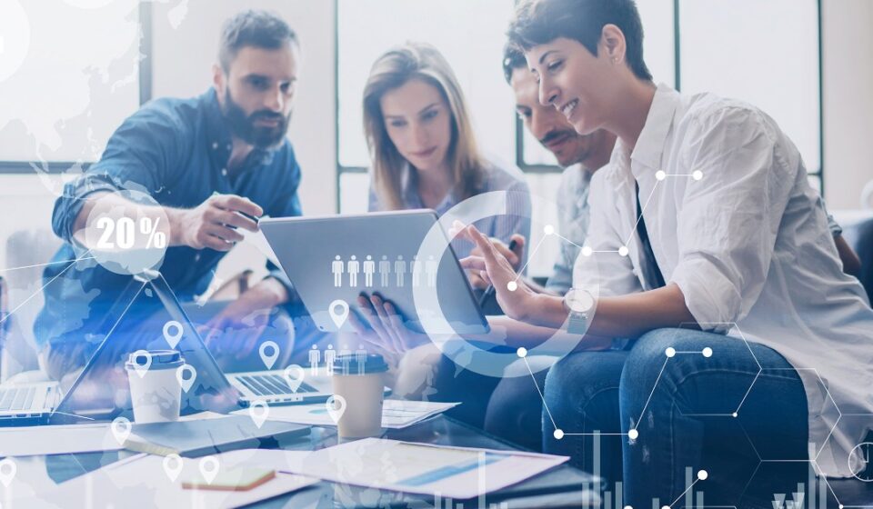 A professional illustration featuring the AWS logo at the center, surrounded by interconnected service icons representing compute, storage, networking, and machine learning capabilities. A team of silhouetted developers stands on a solid foundation built from AWS infrastructure, with upward-trending arrows, shields, and gears symbolizing scalability, security, and operational excellence. Overlaid text reads "How AWS Expertise Can Strengthen Your Technology Team." The image represents the transformative power of AWS Expertise in building resilient, high-performing engineering organizations.